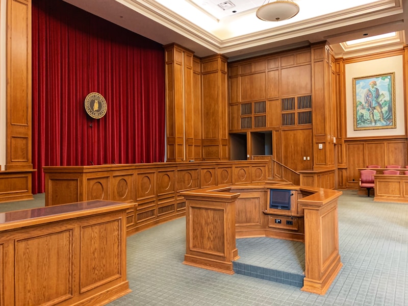 A public hearing room with wood desks and a red curtain